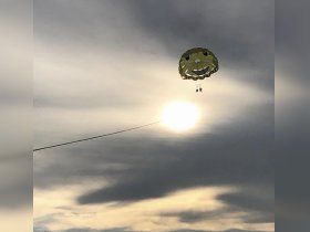 A thrilling parasailing experience captures two adventurers soaring above the water, framed by a stunning sunset — perfect for those seeking excitement on their boating trips.