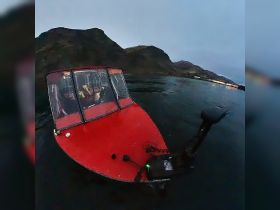A close-up view of a red boat with passengers onboard, set against a dramatic mountainous backdrop — perfect for exploring scenic waters.
