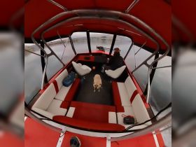 Inside view of a cozy boat cabin featuring comfortable seating and a helm, with a person and a dog enjoying the space.