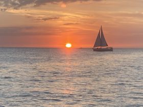 A serene sunset view featuring a sailboat gracefully navigating the waters, creating a picturesque scene perfect for romantic evenings or tranquil escapes.