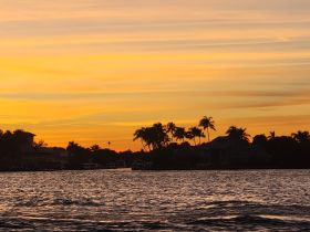A stunning sunset casts vibrant colors over the coastline, creating a picturesque scene perfect for evening boat cruises.