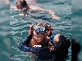 A joyful moment captured as a child enjoys snorkeling in the water, supported by an adult — a perfect family adventure in the ocean.