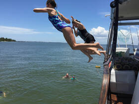 Two girls leap off the side of a boat into the water, capturing the excitement of summer fun and adventure on the water.