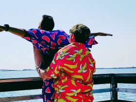 A fun moment captured at the waterfront with two friends in vibrant, playful shirts, enjoying their time together — perfect for memorable summer outings.