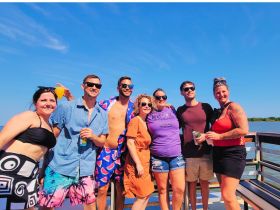 A lively group of friends enjoys a sunny day by the water, celebrating with drinks and smiles — perfect for summer gatherings and fun outings.