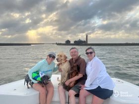 A joyful family poses with their dogs on a boat, enjoying a scenic outing with a beautiful sunset in the background — perfect for memorable moments on the water.
