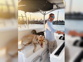 A man enjoys a relaxing moment on a boat with two dogs as the sun sets in the background, capturing the essence of a perfect day on the water.
