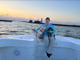 A woman enjoys a serene sunset on a boat with her two dogs, creating a perfect moment of companionship on the water.