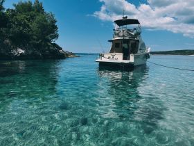 A stunning view of the boat 'Unana' anchored in crystal-clear waters, surrounded by lush greenery and rocky shores — perfect for a serene getaway.