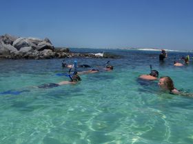 A lively group enjoys snorkeling in crystal-clear waters, exploring the underwater world while surrounded by stunning rock formations.