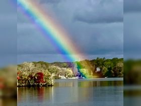 A stunning rainbow arcs over a tranquil waterway, creating a picturesque scene that captures the beauty of nature and the serenity of the surroundings.