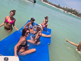 A fun group of friends enjoys a sunny day on a floating mat in crystal-clear waters, perfect for a lively beach party experience.