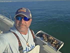 A fisherman takes a selfie on his boat, showcasing a successful catch of fish in the clear ocean waters — perfect for fishing enthusiasts.