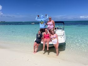 A lively group of friends poses on the beach with their boat in the background, capturing a fun day under the sun — perfect for beach outings and celebrations.
