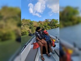 A heartwarming moment on a fishing trip as a mother and her child enjoy quality time together on a boat surrounded by lush greenery.