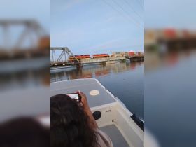 A guest captures a photo of a train crossing a bridge from the deck of a boat, showcasing a unique perspective of waterway travel.