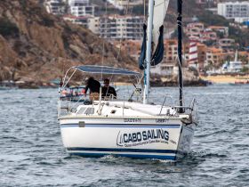 A sailing boat navigates the waters of Cabo San Lucas, showcasing the vibrant coastal scenery and the excitement of ocean adventures.