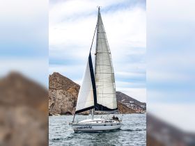 A sailboat named 'Cabo Sailing' navigates the waters near rocky cliffs, showcasing the beauty of sailing adventures in Cabo San Lucas.