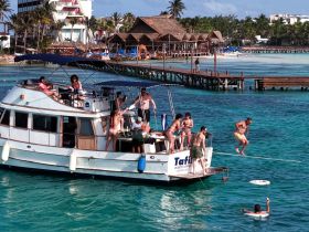 A lively group enjoys a fun day on the water, with guests jumping off the boat and swimming in the clear turquoise sea — perfect for a memorable party experience.