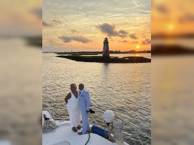 A couple celebrates their special moment aboard a boat at sunset, with a picturesque lighthouse in the background — perfect for romantic getaways or wedding celebrations.