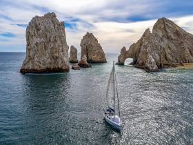 A stunning view of a sailboat navigating near the iconic rock formations of Cabo San Lucas, showcasing the breathtaking coastal scenery.