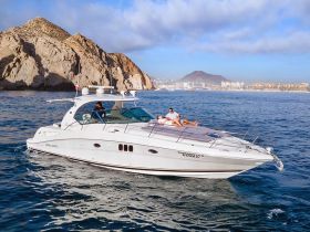 A couple enjoys sunbathing on the deck of a luxurious yacht as it cruises along a stunning coastline, perfect for a relaxing day on the water.