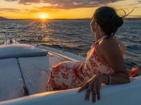 A woman enjoys a stunning sunset view from the deck of a yacht, creating a perfect backdrop for romantic cruises or special celebrations on the water.