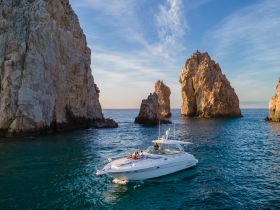 A stunning yacht navigates through the iconic rock formations at sunset, showcasing the breathtaking coastline — a perfect moment for adventure seekers.