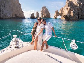 A joyful family poses on the bow of a boat in Cabo San Lucas, with stunning rock formations in the background — a perfect moment capturing the beauty of their ocean adventure.