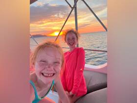 Two joyful children smile for the camera aboard a boat as the sun sets over the horizon, capturing a perfect moment of happiness on the water.