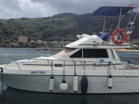 A side view of the 'Magic Boat' docked, showcasing its sleek design against a scenic backdrop of hills and buildings.