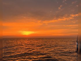 A stunning sunset over the ocean with a boat visible in the foreground, creating a picturesque scene perfect for evening cruises.