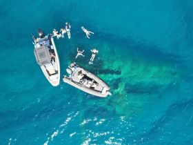Aerial view of a lively group enjoying snorkeling and swimming around two boats in crystal-clear waters, showcasing the perfect day on the water.
