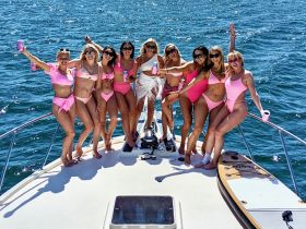 A lively group of friends celebrates aboard a yacht, dressed in matching pink swimsuits, perfect for a bachelorette party or summer getaway on the water.