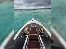 Two friends relax and sunbathe on the deck of a boat, surrounded by stunning turquoise waters — a perfect day for leisure and enjoyment on the water.