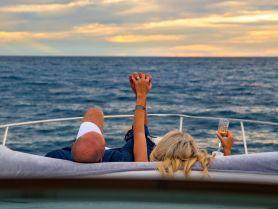 A couple enjoys a romantic sunset on a yacht, holding hands and toasting with cocktails — an ideal moment for love and celebration on the water.