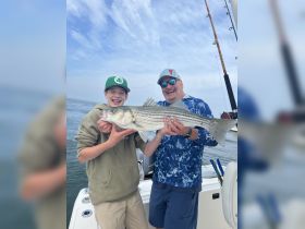 A joyful moment captured as a child and an adult proudly display their impressive catch while fishing on a boat — a perfect memory of a fun day on the water.