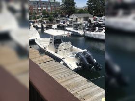 A center console boat docked at a marina, showcasing its sleek design and powerful twin engines — perfect for fishing or day cruising.