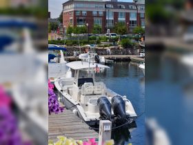 A sleek center console boat docked at a marina, showcasing its powerful twin engines and spacious seating — perfect for fishing or day cruising.