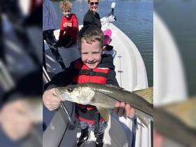 A joyful child proudly holds up a fish while fishing with family on a boat, capturing a memorable moment of fun and adventure on the water.