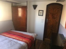 Cozy interior cabin featuring a double bed with a colorful blanket, wooden doors, and charming decor, perfect for relaxing on a boat getaway.