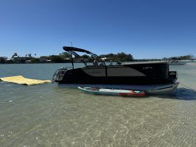 A sleek pontoon boat is docked in shallow waters, showcasing its elegant design against a clear blue sky — perfect for leisurely outings or family fun on the water.