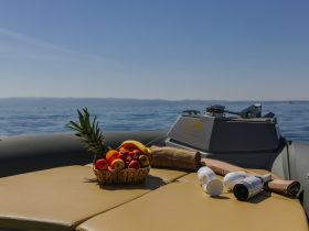 A beautifully arranged basket of fresh fruits sits on the deck of a boat, perfect for a relaxing day on the water. Enjoy the sun and refreshments while cruising.
