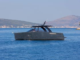A sleek yacht glides through calm waters, showcasing its modern design against a picturesque backdrop of hills and coastal scenery.