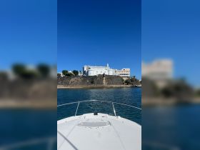 A clear view from the front of a boat approaching a historic landmark, showcasing the beautiful architecture against a bright blue sky — perfect for sightseeing tours.