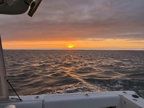 A stunning sunset view from the deck of a boat, showcasing the tranquil ocean waves and vibrant sky — perfect for evening cruises.
