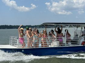 A lively group of friends celebrates on a pontoon boat, enjoying a sunny day on the water — perfect for summer parties and fun outings.