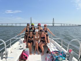 A fun group of friends celebrates a bachelorette party aboard a boat, showcasing their vibrant outfits and excitement against the backdrop of a stunning bridge.