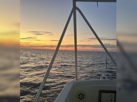 A serene sunset view from the deck of a boat, showcasing the tranquil ocean waters and a beautiful sky, perfect for evening cruises.