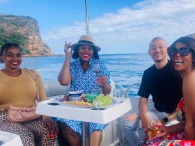 A joyful group enjoys a delightful meal and drinks on a boat, surrounded by stunning water views — perfect for celebrations and memorable outings.